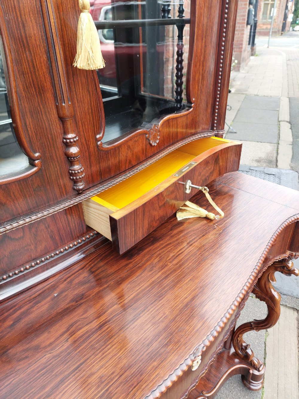 A two-tier Biedermeier rosewood display cabinet featuring a glazed upper section with a carved cresting above a two-door cupboard base. View VII