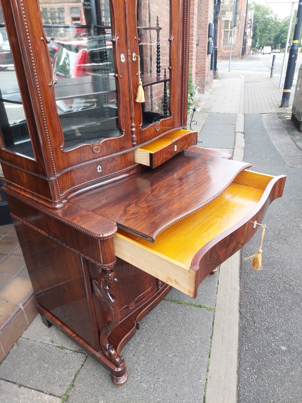 A two-tier Biedermeier rosewood display cabinet featuring a glazed upper section with a carved cresting above a two-door cupboard base. View VIII