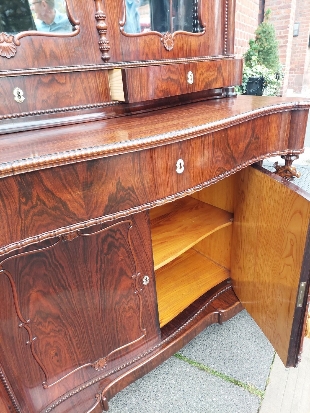 A two-tier Biedermeier rosewood display cabinet featuring a glazed upper section with a carved cresting above a two-door cupboard base. View IX