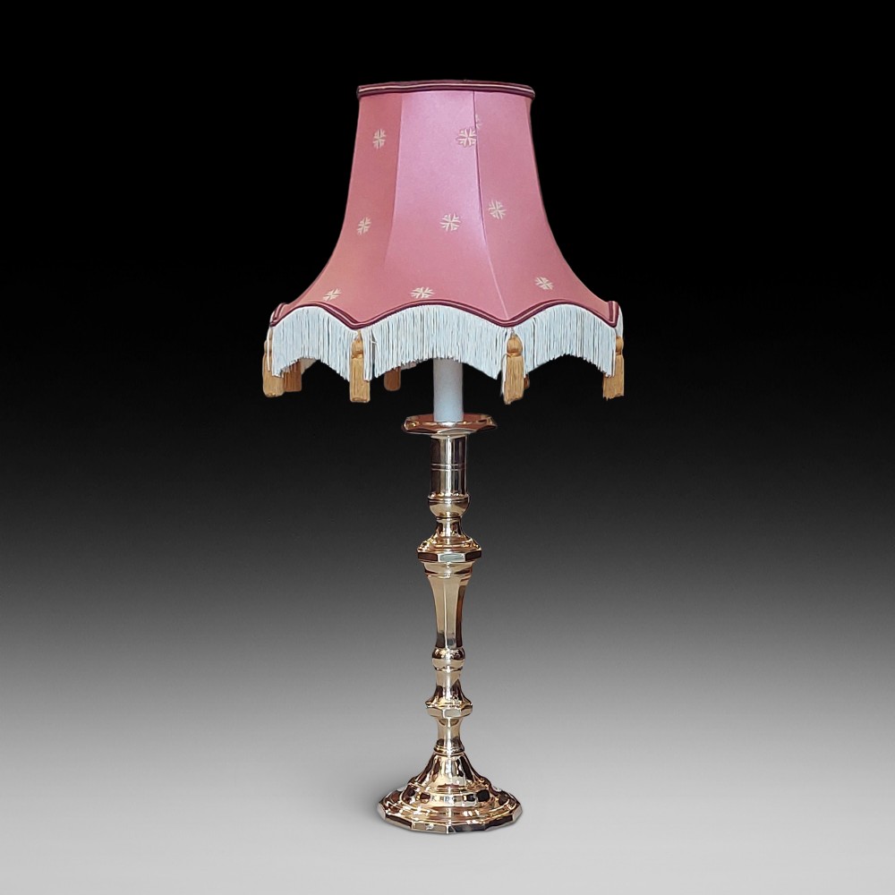 A Victorian turned brass candlestick table lamp featuring a rose pink embroidered lampshade with fringe and tassel trim.