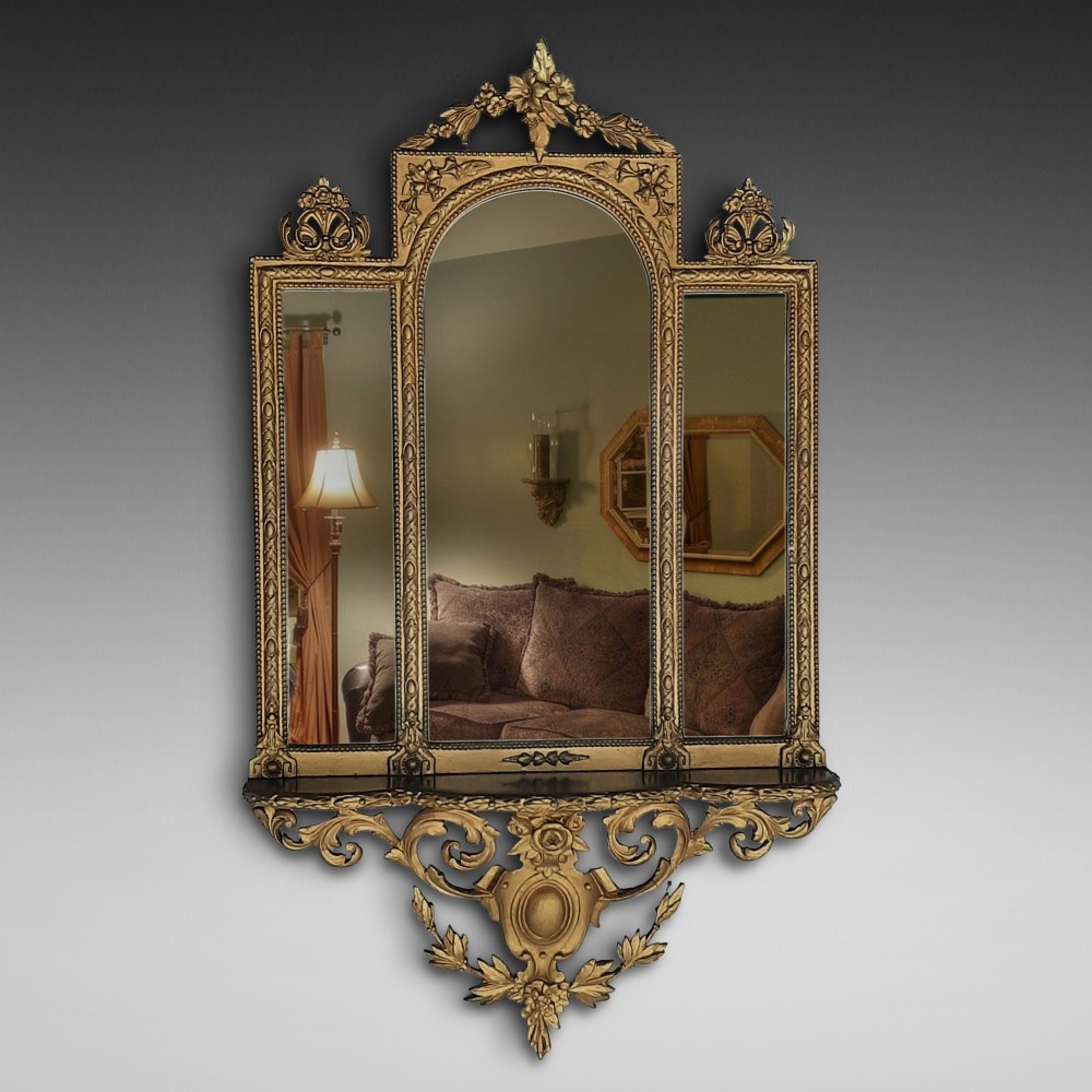 A late nineteenth-century three-panel gilt wall mirror featuring an arched central plate, intricate carved floral cresting, and an integrated base shelf.