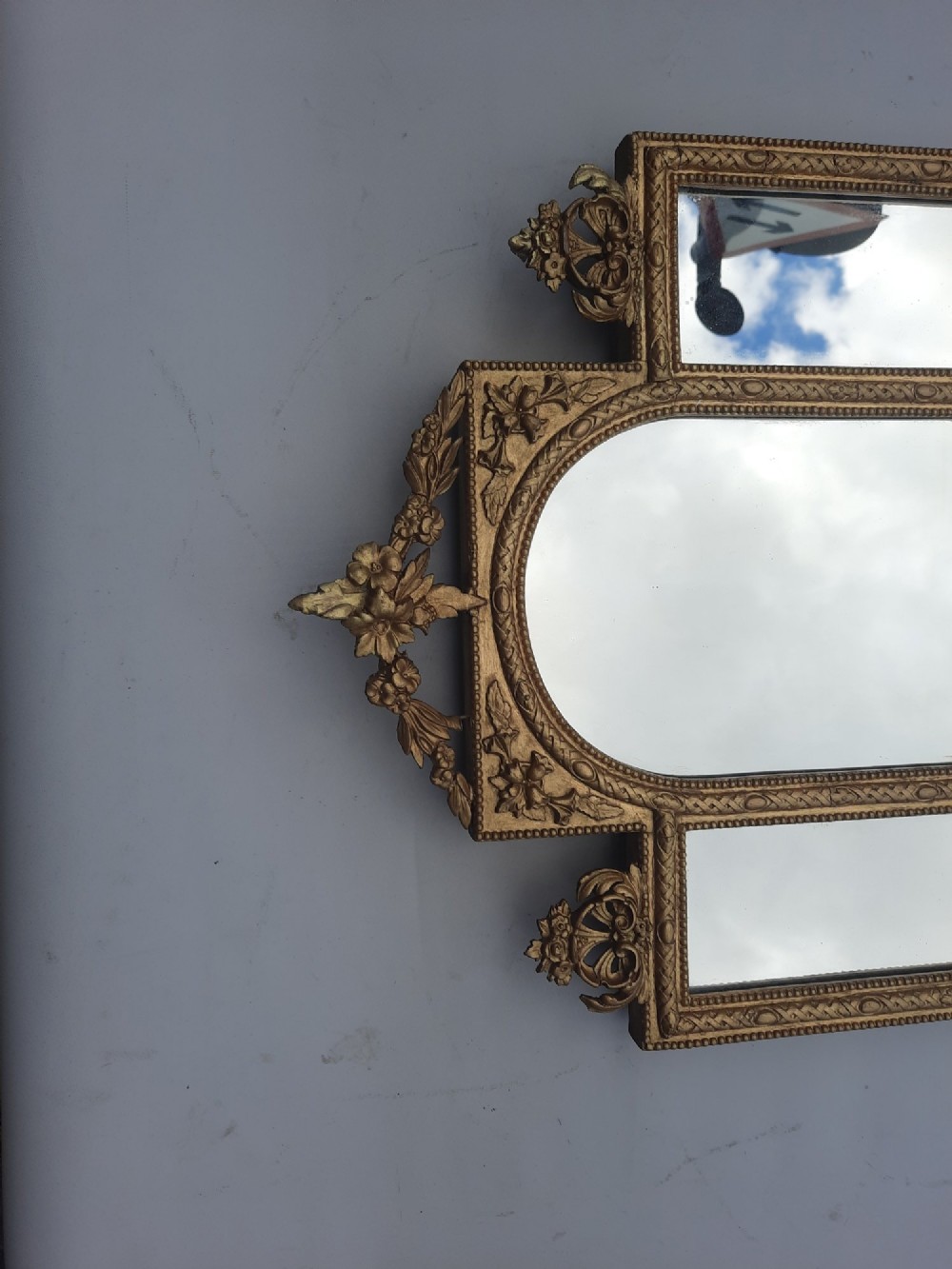 A late nineteenth-century three-panel gilt wall mirror featuring an arched central plate, intricate carved floral cresting, and an integrated base shelf. View II