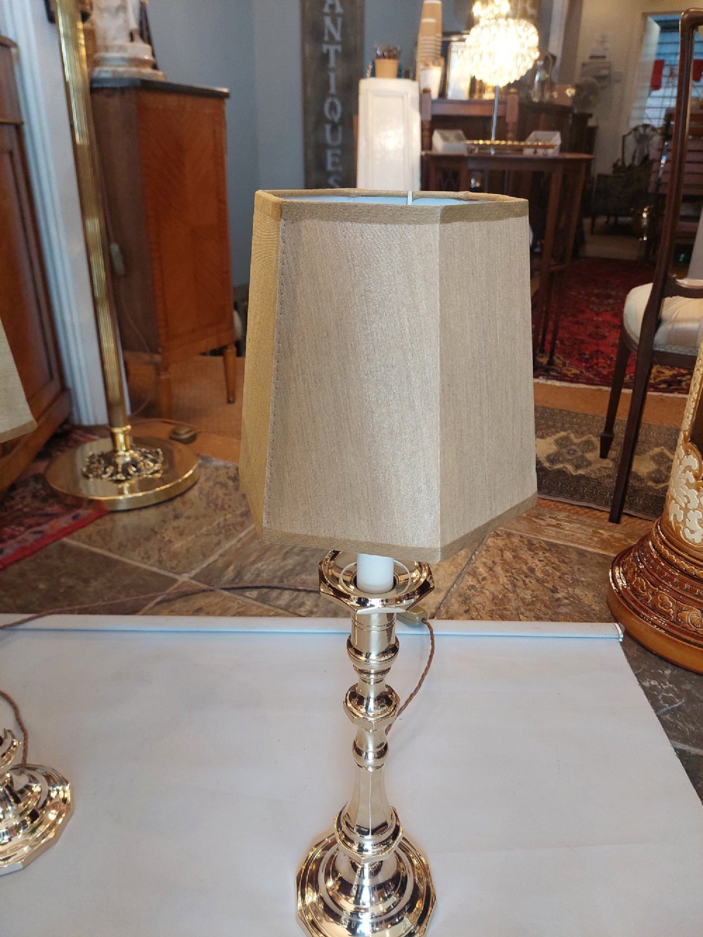 A pair of polished Victorian brass candlestick table lamps fitted with hexagonal beige fabric shades. View VI