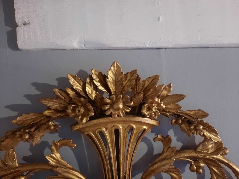 An oval giltwood wall mirror featuring an intricate carved urn cresting, acanthus leaf foliage, and a beaded inner frame border. View V