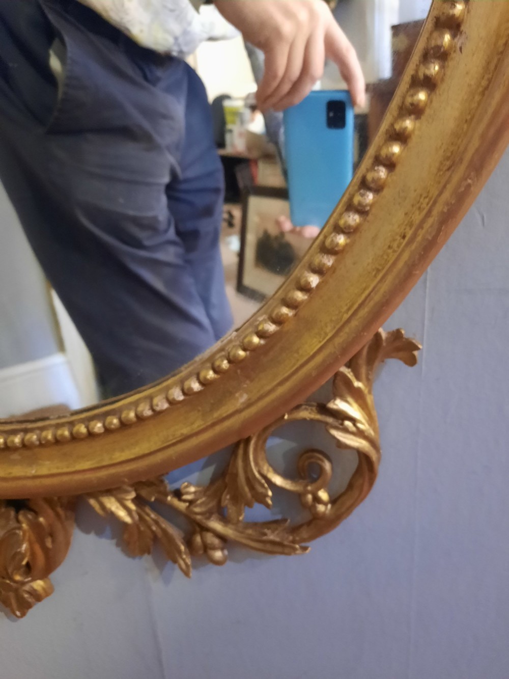 An oval giltwood wall mirror featuring an intricate carved urn cresting, acanthus leaf foliage, and a beaded inner frame border. View VII