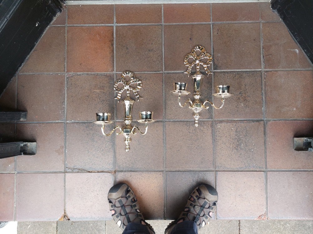 A pair of polished brass double-arm wall sconces featuring ribbon bow top motifs, urn-shaped central stems, and scrolling candle branches. View II