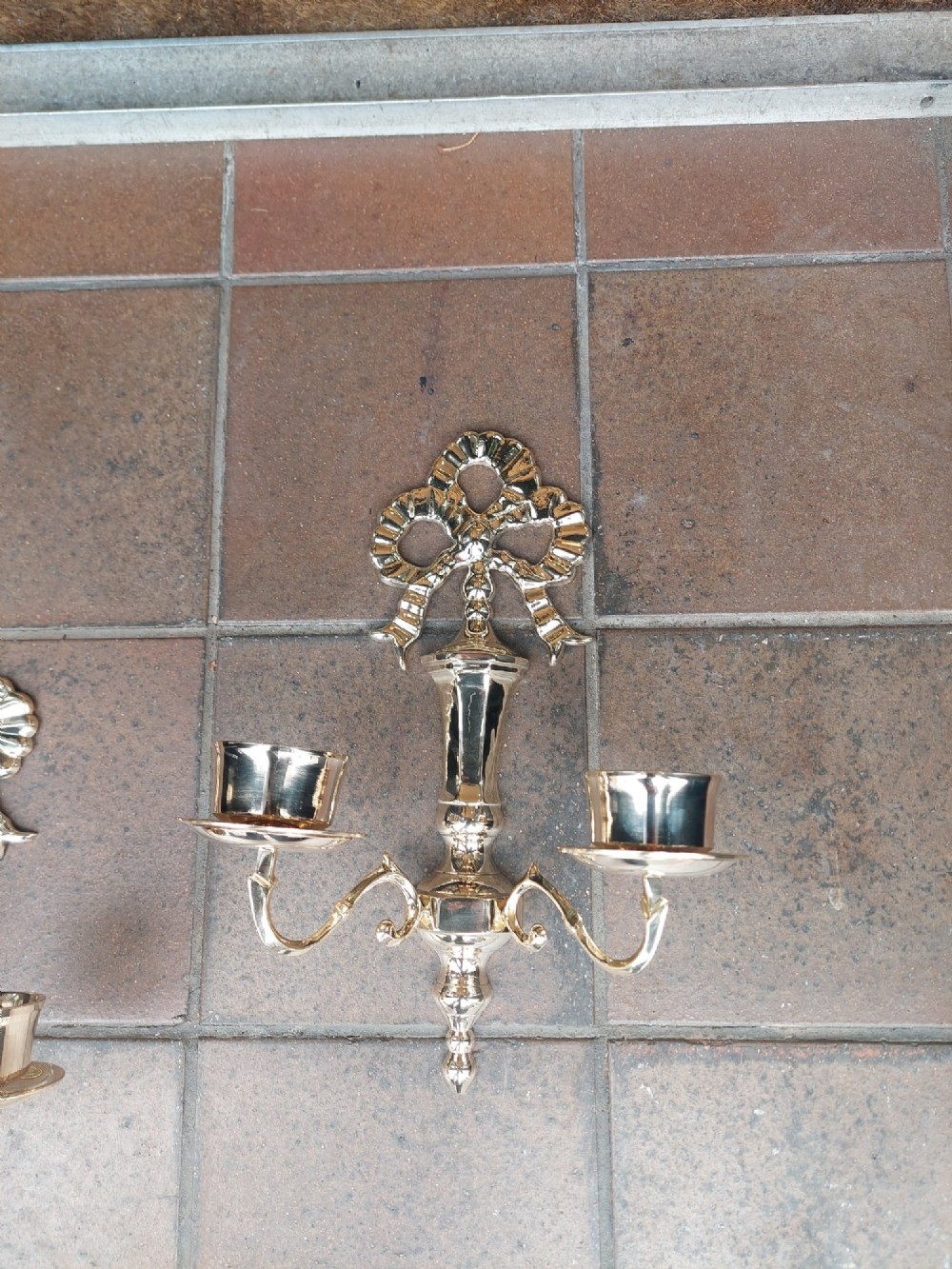 A pair of polished brass double-arm wall sconces featuring ribbon bow top motifs, urn-shaped central stems, and scrolling candle branches. View IV