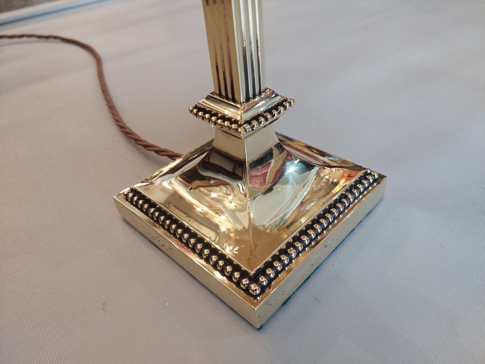 An Edwardian Neoclassical Revival silver-plated table lamp featuring a fluted column stem, square stepped base, and a cream fabric shade adorned with beaded fringe. View V