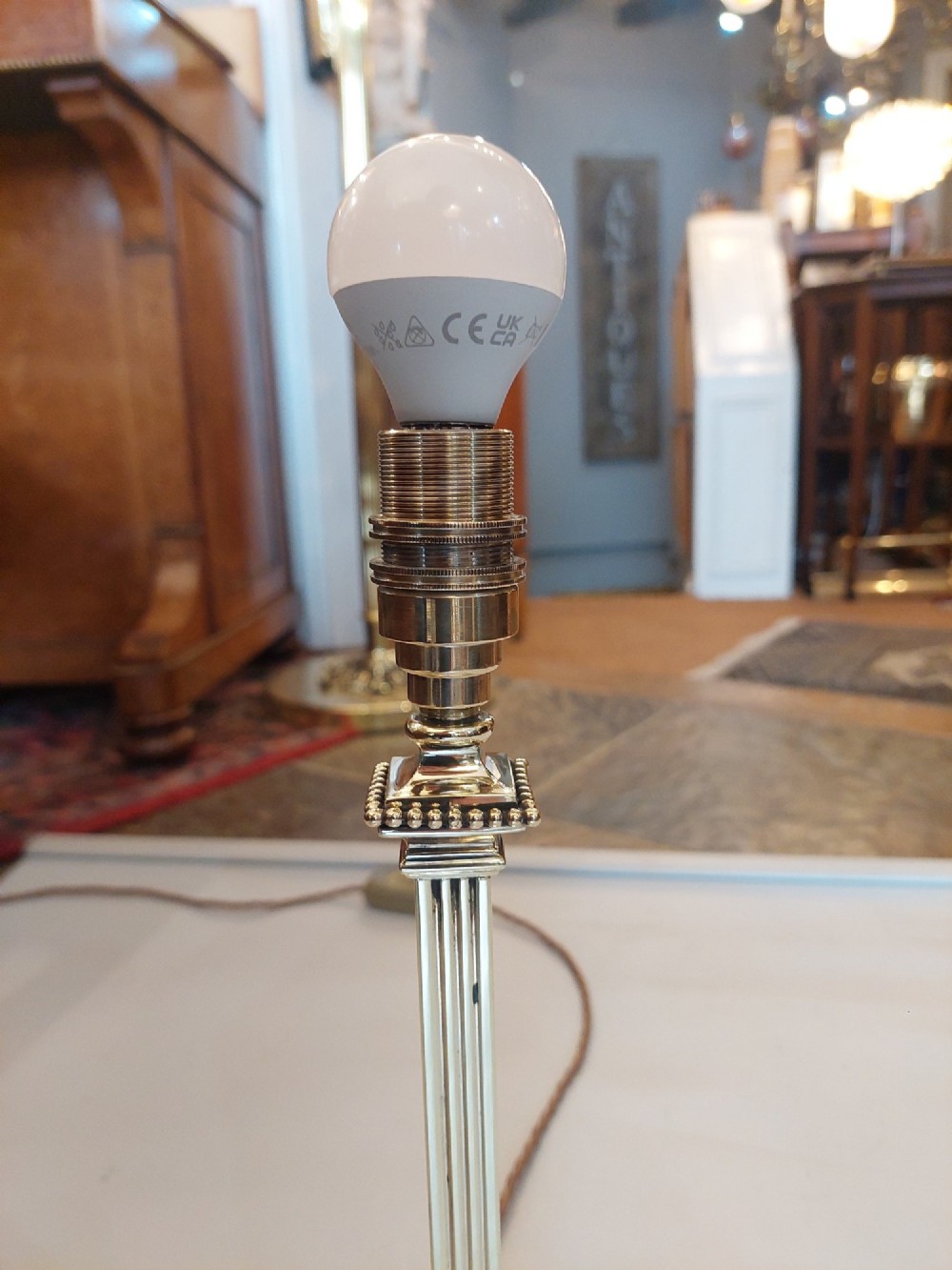 An Edwardian Neoclassical Revival silver-plated table lamp featuring a fluted column stem, square stepped base, and a cream fabric shade adorned with beaded fringe. View VII