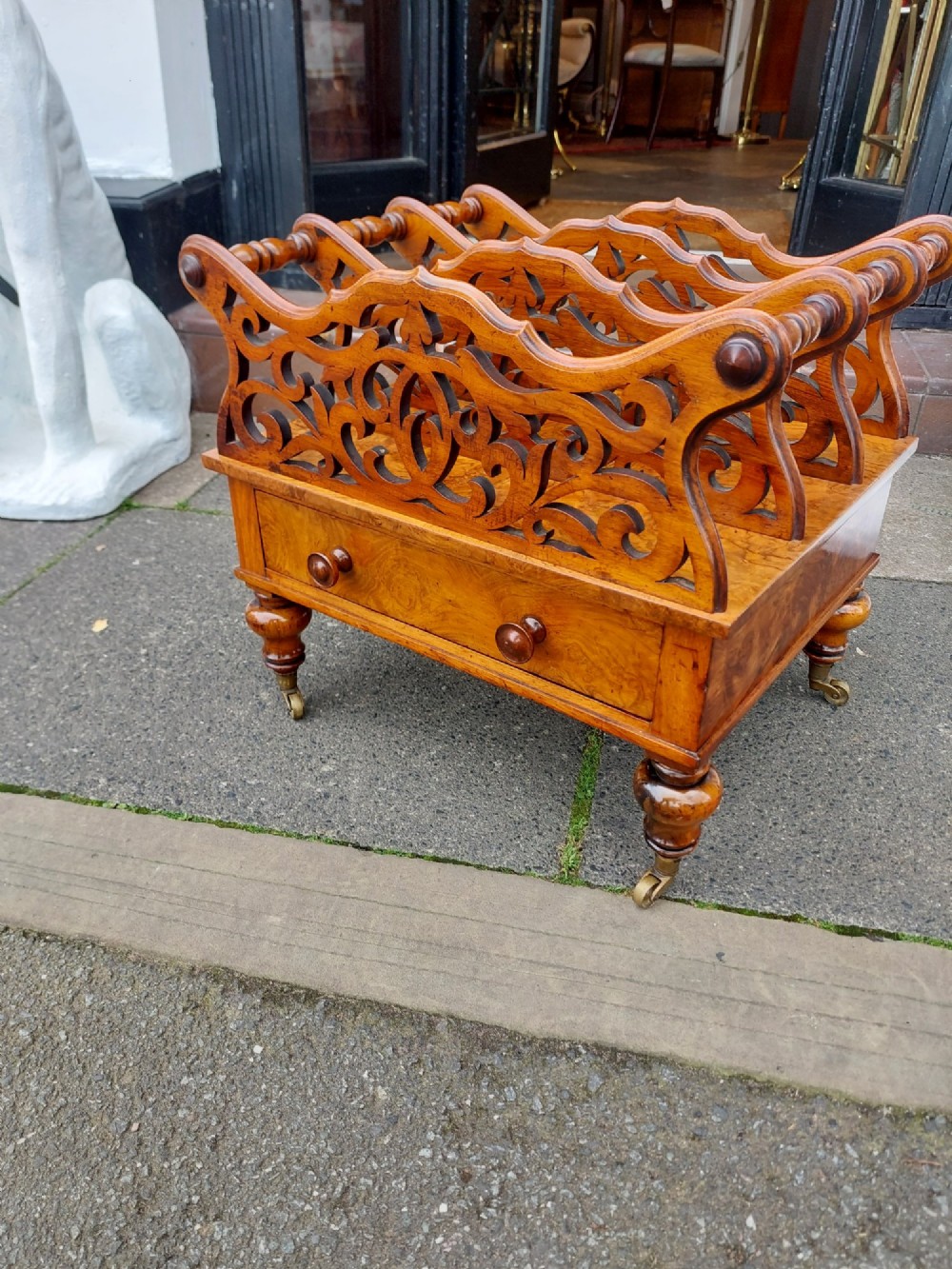 A High Victorian burr walnut Canterbury featuring four open compartments with fretwork dividers above a single drawer with turned legs on brass castors. View III