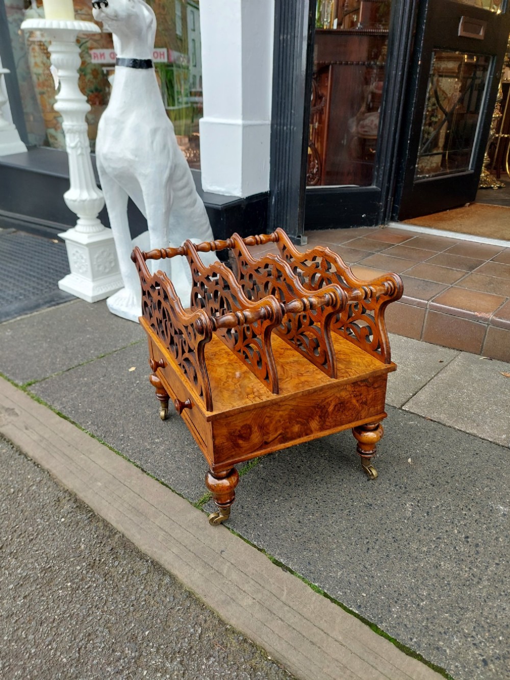 A High Victorian burr walnut Canterbury featuring four open compartments with fretwork dividers above a single drawer with turned legs on brass castors. View IV