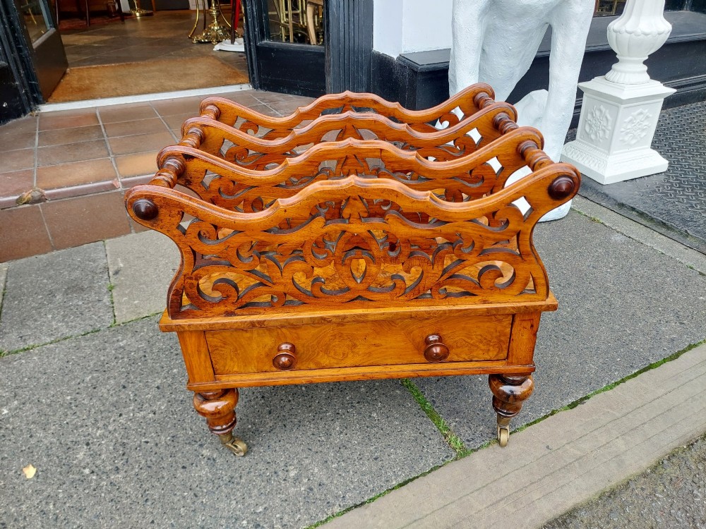 A High Victorian burr walnut Canterbury featuring four open compartments with fretwork dividers above a single drawer with turned legs on brass castors. View V