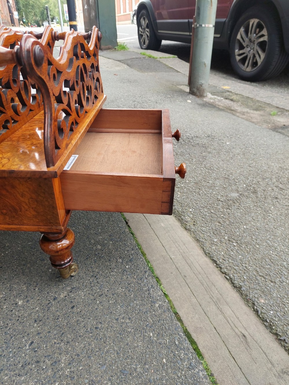 A High Victorian burr walnut Canterbury featuring four open compartments with fretwork dividers above a single drawer with turned legs on brass castors. View VI