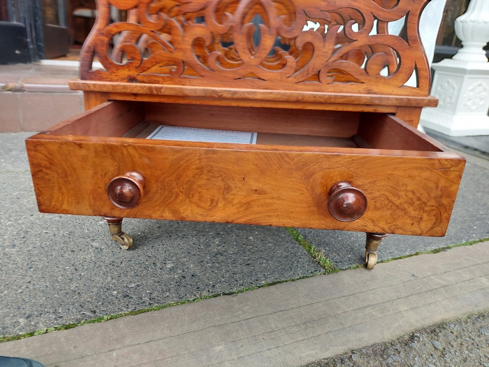 A High Victorian burr walnut Canterbury featuring four open compartments with fretwork dividers above a single drawer with turned legs on brass castors. View VII
