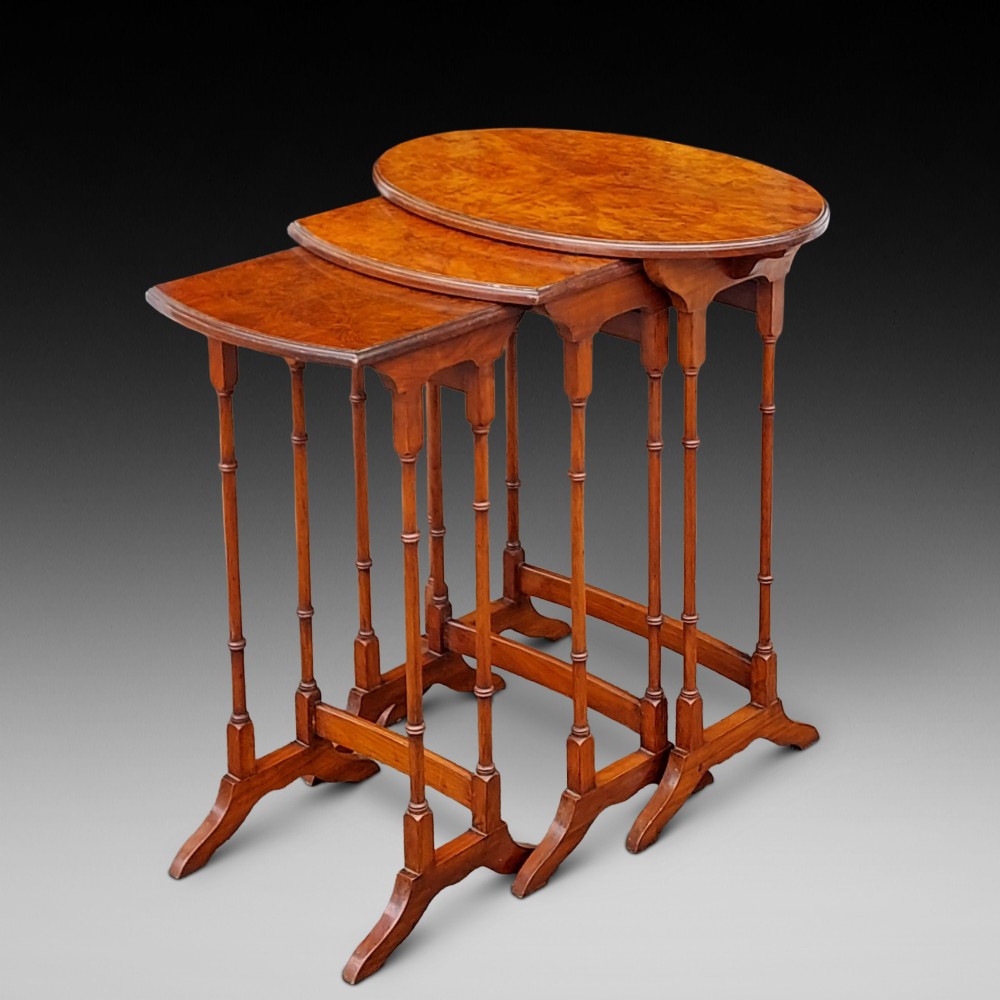 A set of three Edwardian nesting tables crafted from burr walnut with slender turned legs, stretcher supports, and shaped tops.
