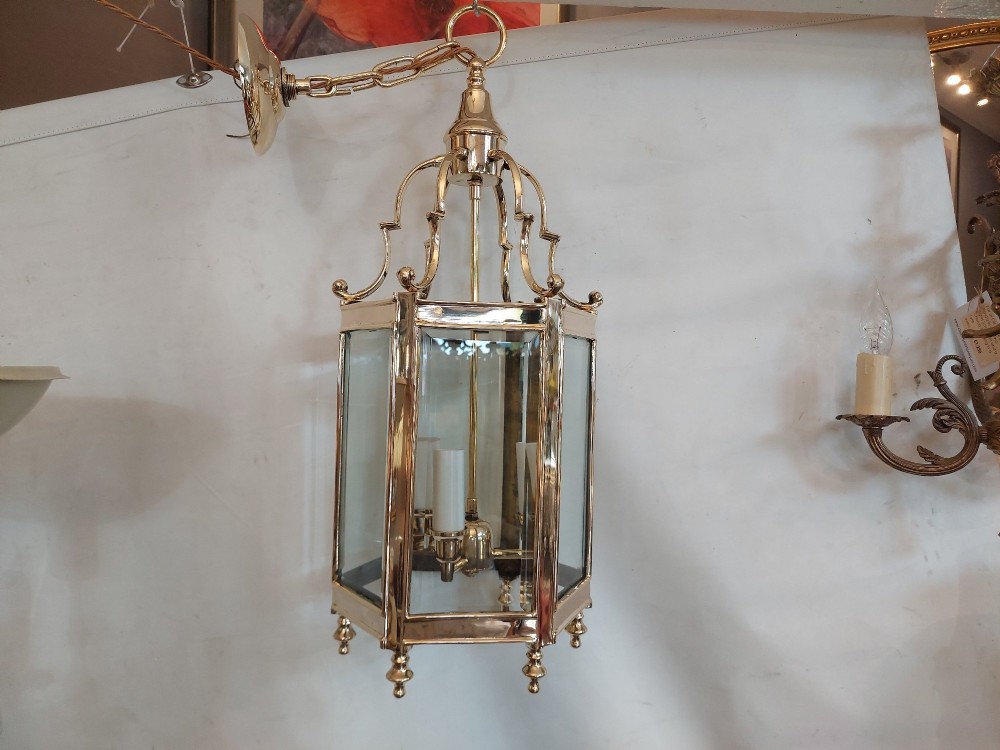 A hexagonal polished brass ceiling lantern with clear glass side panels, scrolled top canopy, and turned bottom finials. View II