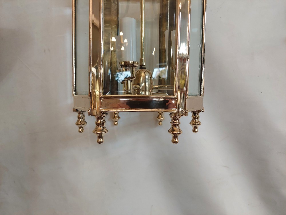A hexagonal polished brass ceiling lantern with clear glass side panels, scrolled top canopy, and turned bottom finials. View III