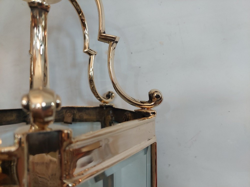 A hexagonal polished brass ceiling lantern with clear glass side panels, scrolled top canopy, and turned bottom finials. View VI