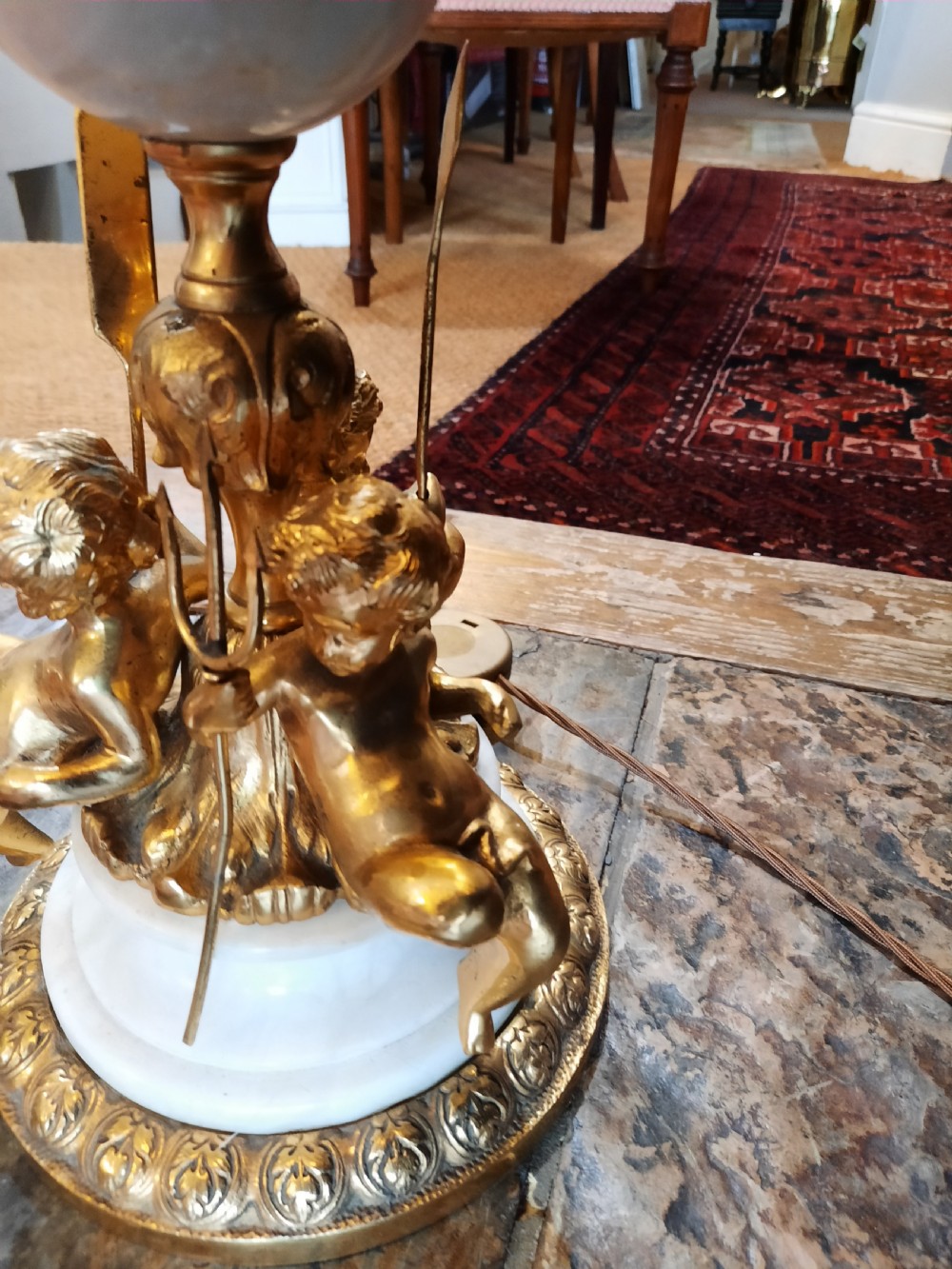 A three-piece antique lamp set featuring two tall standard lamps and one table lamp with ornate gilt cherub bases, alabaster spheres, and fringed cream domed shades. View VII