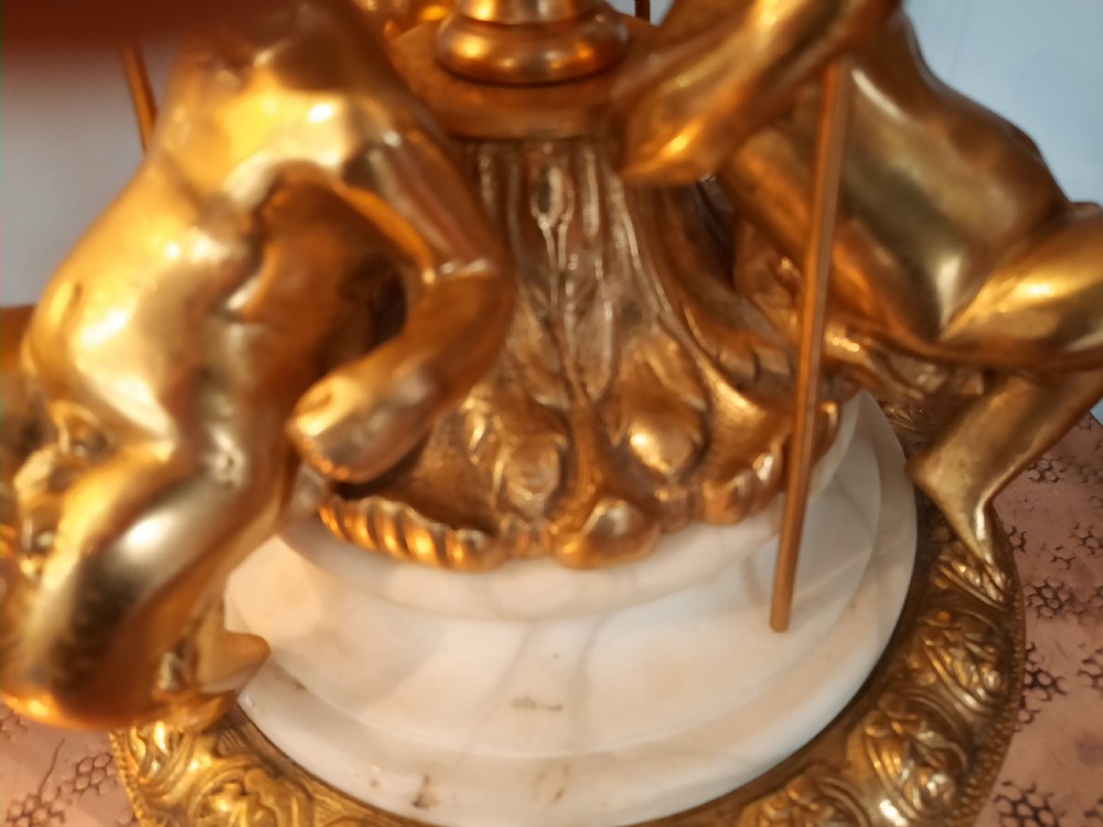 A three-piece antique lamp set featuring two tall standard lamps and one table lamp with ornate gilt cherub bases, alabaster spheres, and fringed cream domed shades. View X