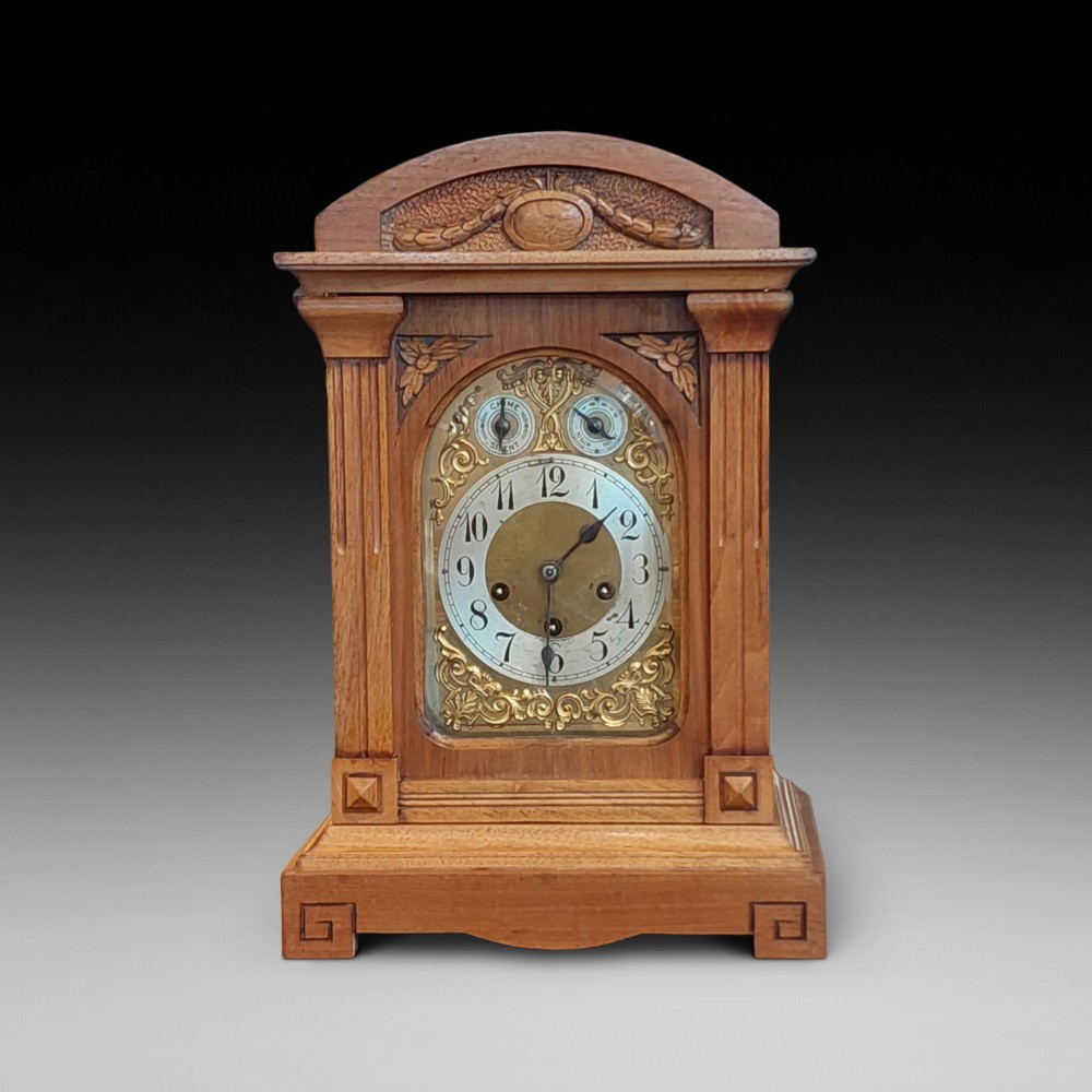 An antique oak mantel clock featuring carved columns, an arched brass dial with silvered numerals, and two small subsidiary dials.