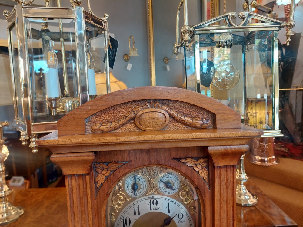 An antique oak mantel clock featuring carved columns, an arched brass dial with silvered numerals, and two small subsidiary dials. View III