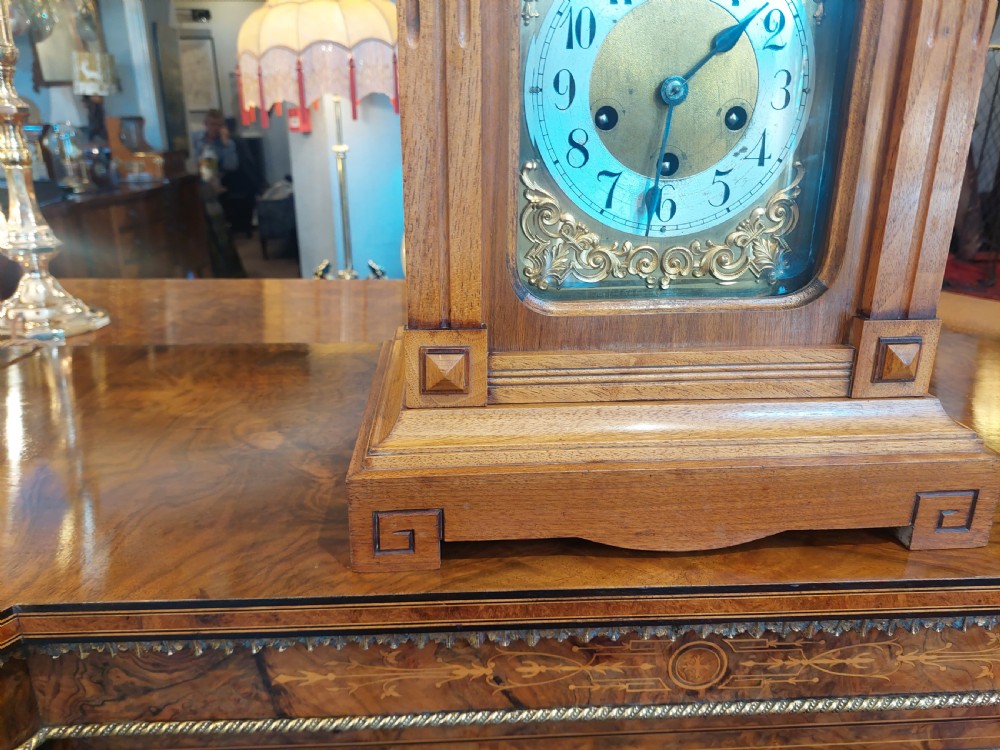 An antique oak mantel clock featuring carved columns, an arched brass dial with silvered numerals, and two small subsidiary dials. View IV