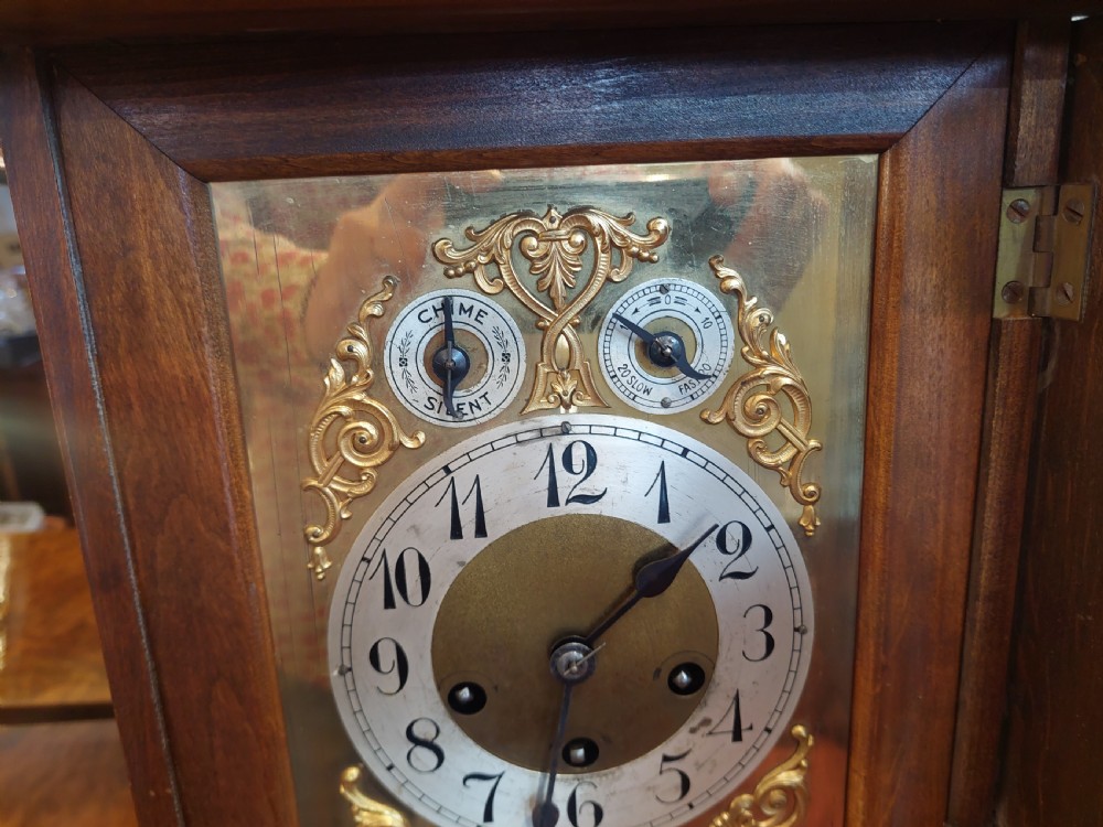 An antique oak mantel clock featuring carved columns, an arched brass dial with silvered numerals, and two small subsidiary dials. View V