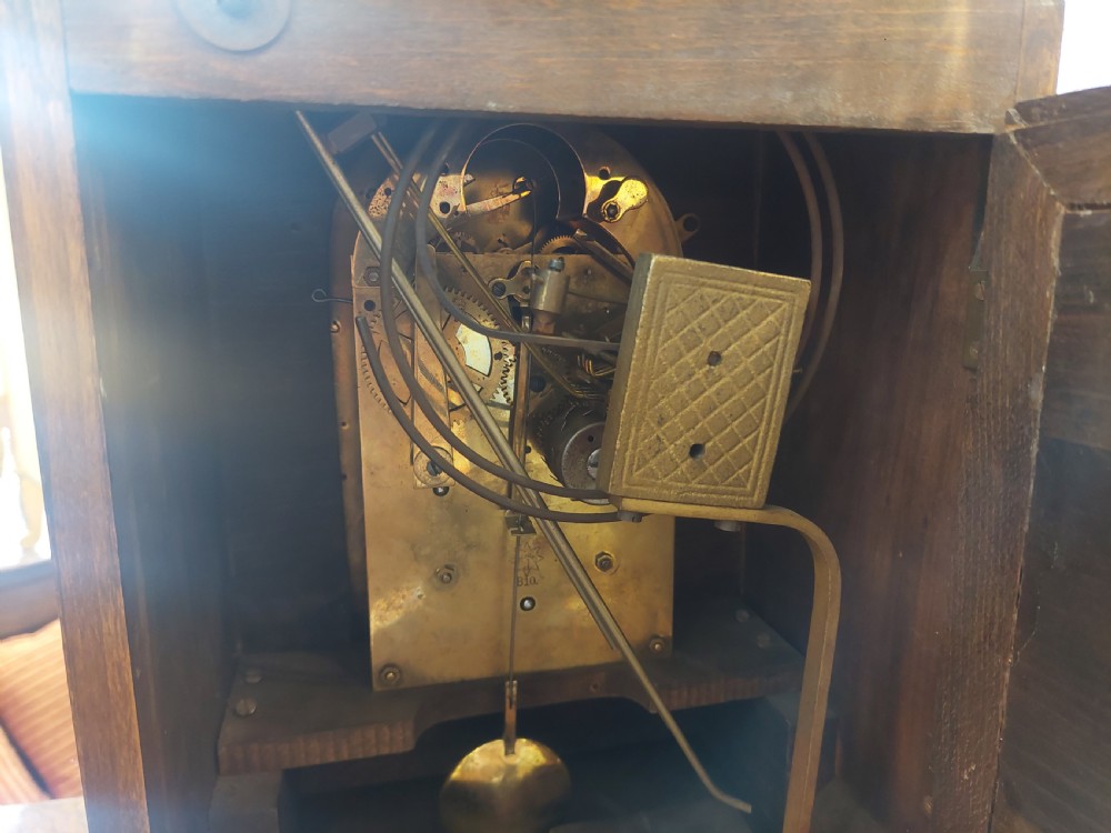 An antique oak mantel clock featuring carved columns, an arched brass dial with silvered numerals, and two small subsidiary dials. View VI