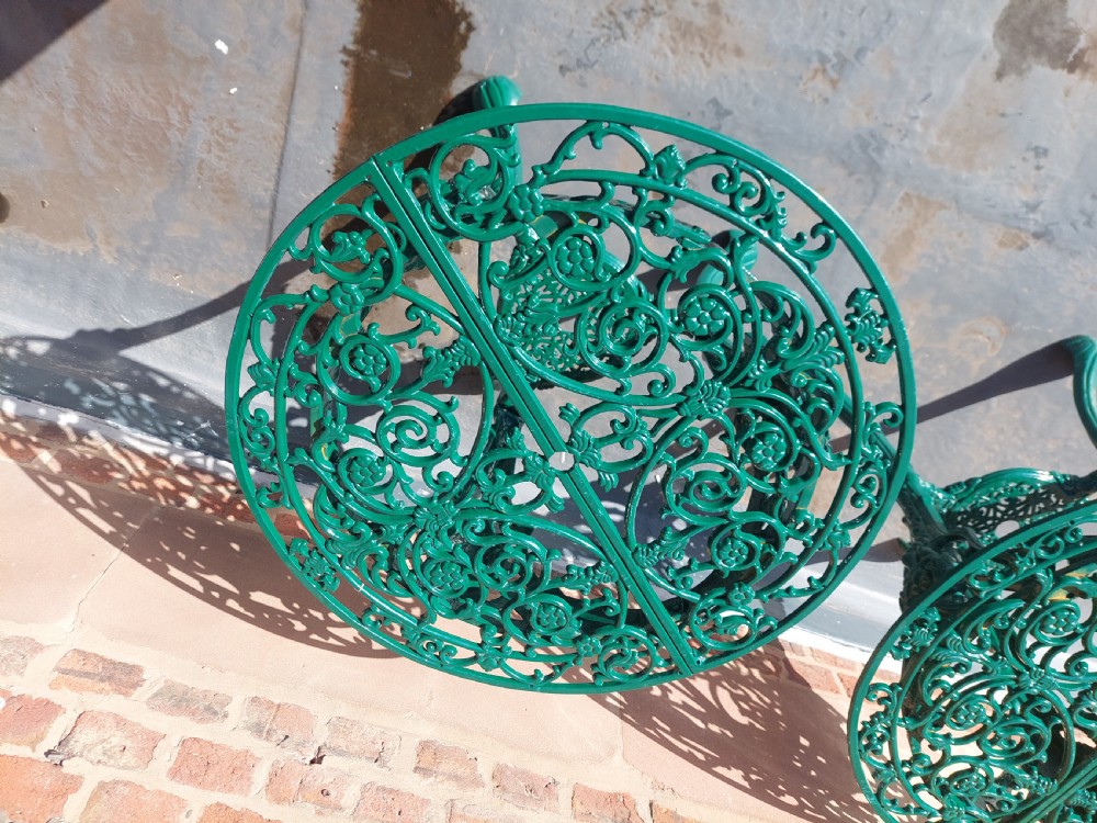 A pair of circular green painted cast iron garden tables featuring pierced foliate tops, mask-adorned legs, and a lower triangular stretcher shelf. View III
