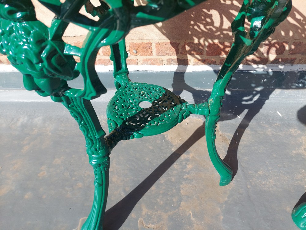 A pair of circular green painted cast iron garden tables featuring pierced foliate tops, mask-adorned legs, and a lower triangular stretcher shelf. View VI