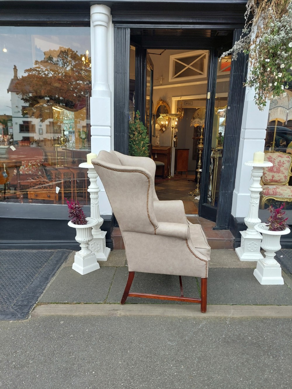 A Victorian wingback armchair upholstered in off-white leather with scrolled arms and dark mahogany legs connected by stretchers. View V
