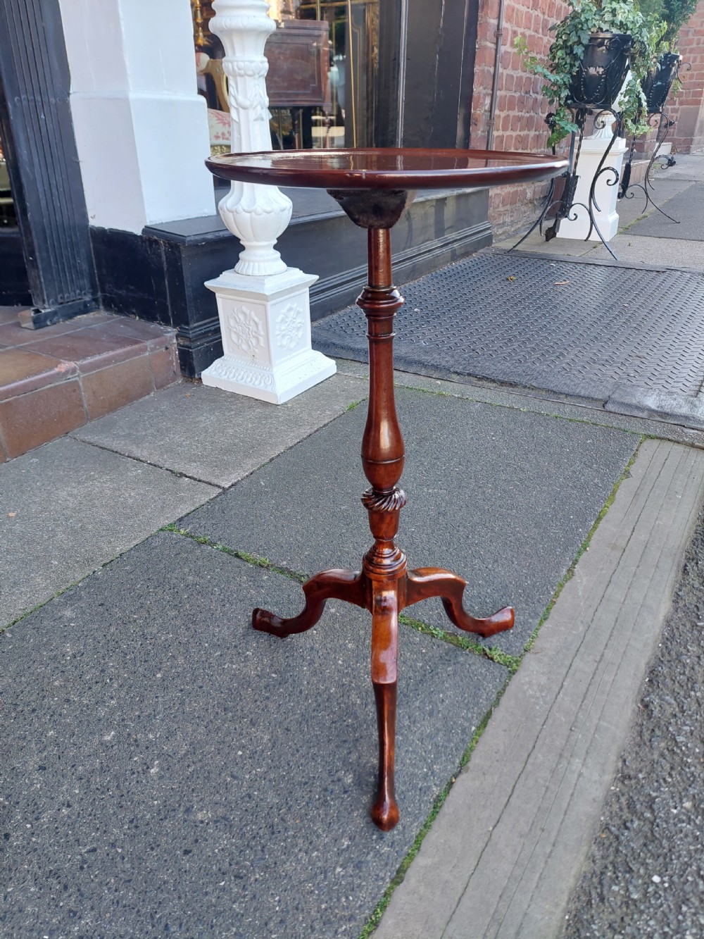 An Edwardian mahogany wine table featuring a polished circular top, turned central column, and three cabriole tripod legs. View V