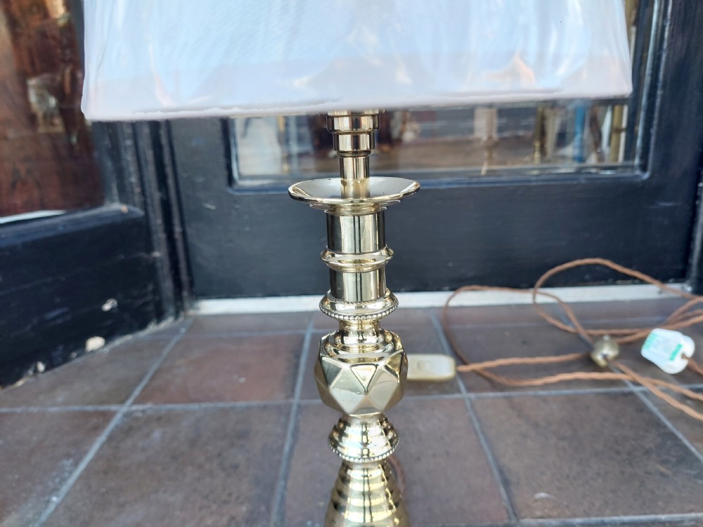 A pair of turned brass Edwardian candlestick table lamps fitted with white pleated lampshades. View IV