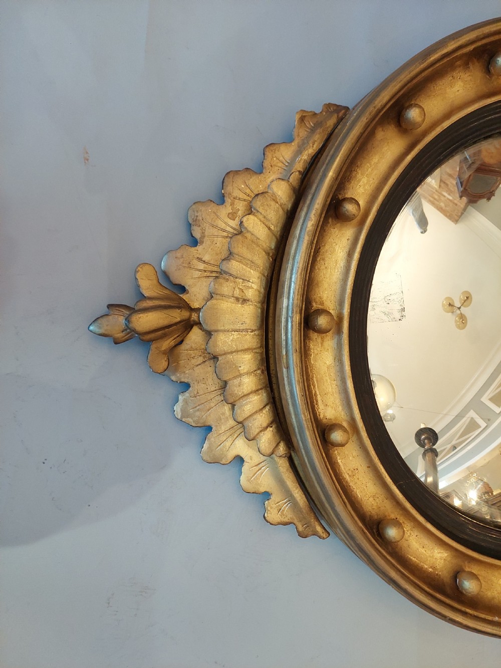A circular Regency giltwood convex wall mirror featuring a carved eagle surmount, spherical balls around the moulded frame, a black reeded slip, and an acanthus leaf apron. View II