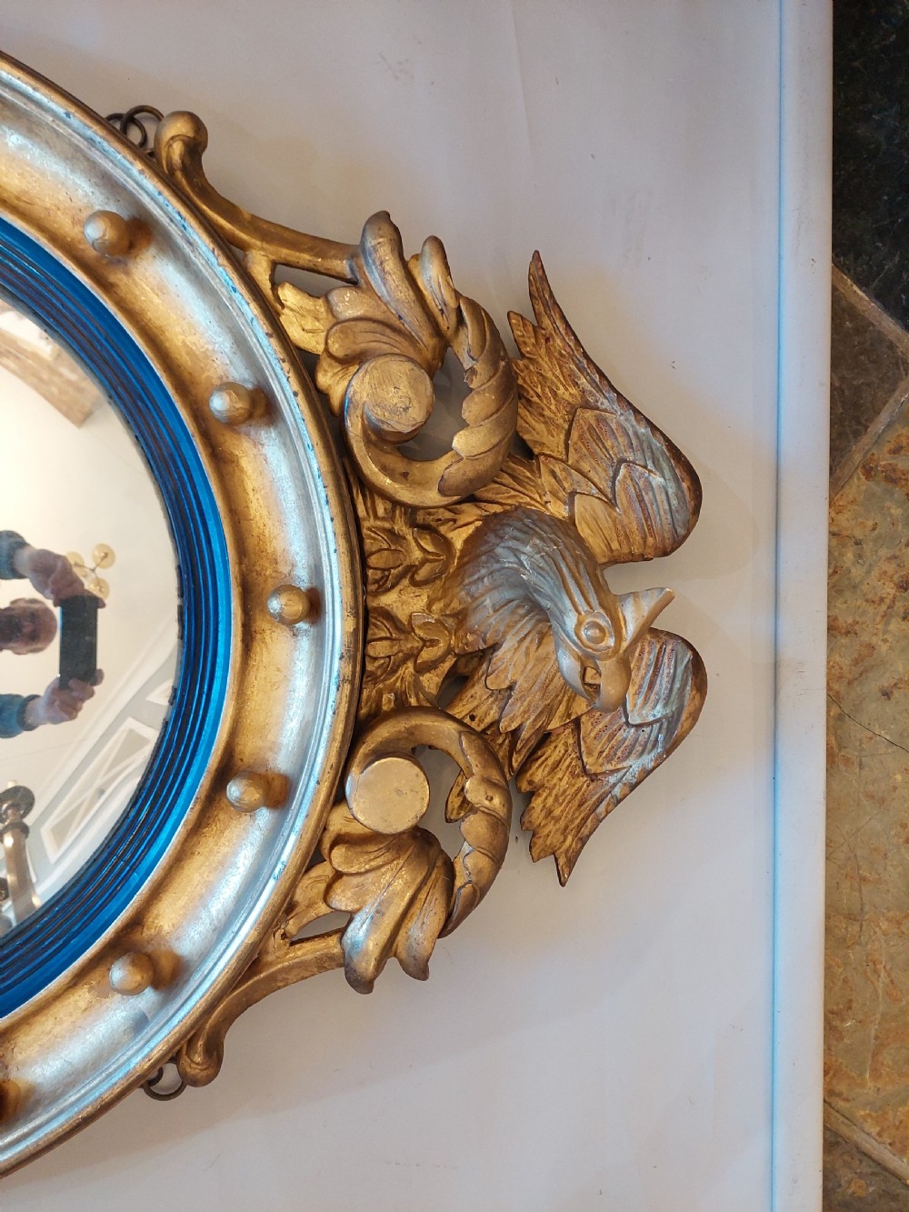 A circular Regency giltwood convex wall mirror featuring a carved eagle surmount, spherical balls around the moulded frame, a black reeded slip, and an acanthus leaf apron. View III