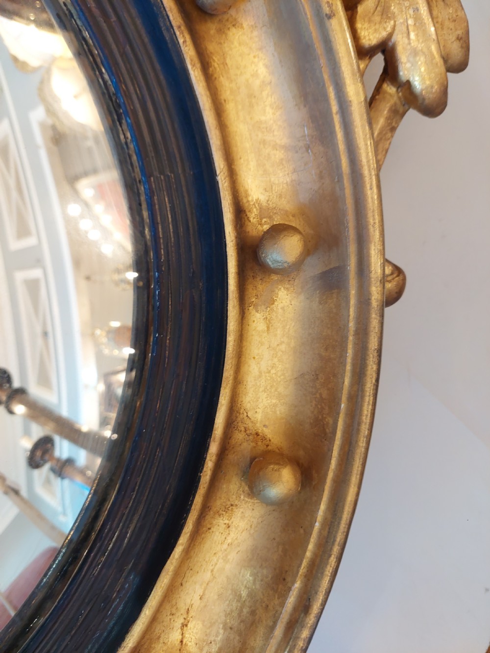 A circular Regency giltwood convex wall mirror featuring a carved eagle surmount, spherical balls around the moulded frame, a black reeded slip, and an acanthus leaf apron. View V