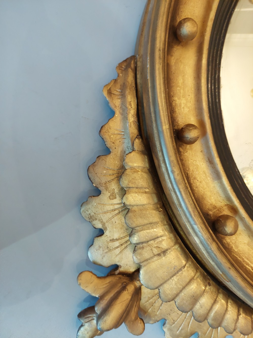 A circular Regency giltwood convex wall mirror featuring a carved eagle surmount, spherical balls around the moulded frame, a black reeded slip, and an acanthus leaf apron. View VI