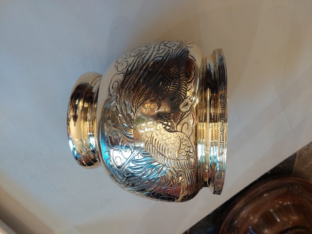 A rounded polished brass Japanese jardiniere with hand-chased relief dragons and clouds, resting on a stepped base. View IV