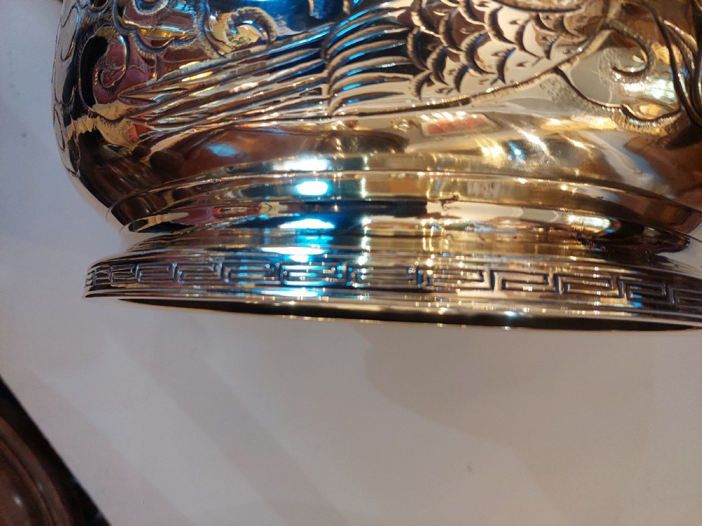 A rounded polished brass Japanese jardiniere with hand-chased relief dragons and clouds, resting on a stepped base. View VI