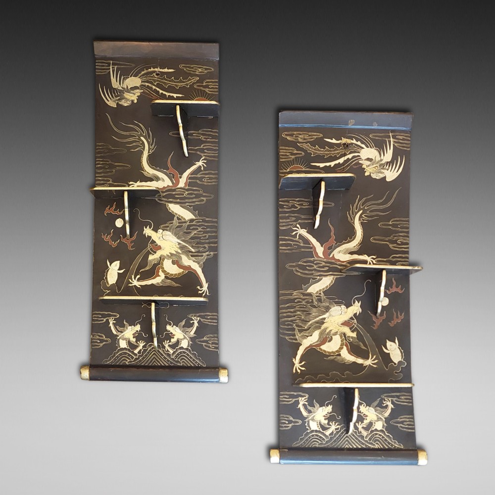 A pair of black lacquered wall shelves featuring scroll end caps and hand-painted gilt dragon and phoenix motifs with stepped display brackets.