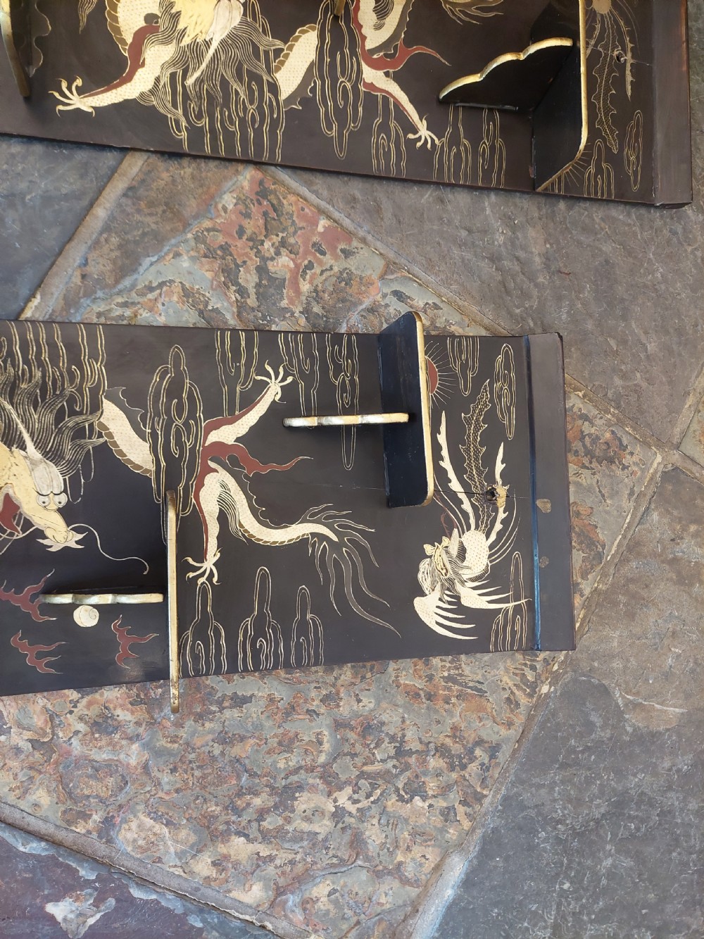 A pair of black lacquered wall shelves featuring scroll end caps and hand-painted gilt dragon and phoenix motifs with stepped display brackets. View V