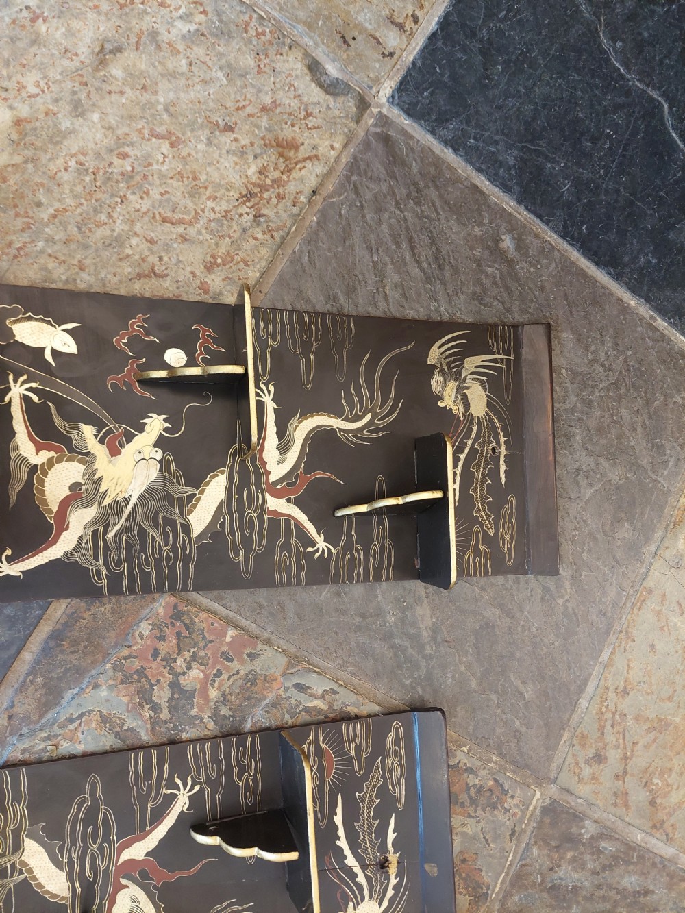 A pair of black lacquered wall shelves featuring scroll end caps and hand-painted gilt dragon and phoenix motifs with stepped display brackets. View VI