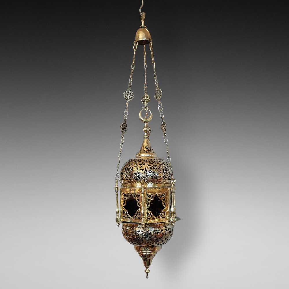A hanging polished brass lantern featuring intricate pierced fretwork, dark glass insert panels, and three suspension chains topped with a crescent moon motif.