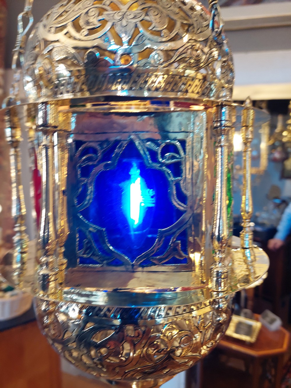 A hanging polished brass lantern featuring intricate pierced fretwork, dark glass insert panels, and three suspension chains topped with a crescent moon motif. View XI
