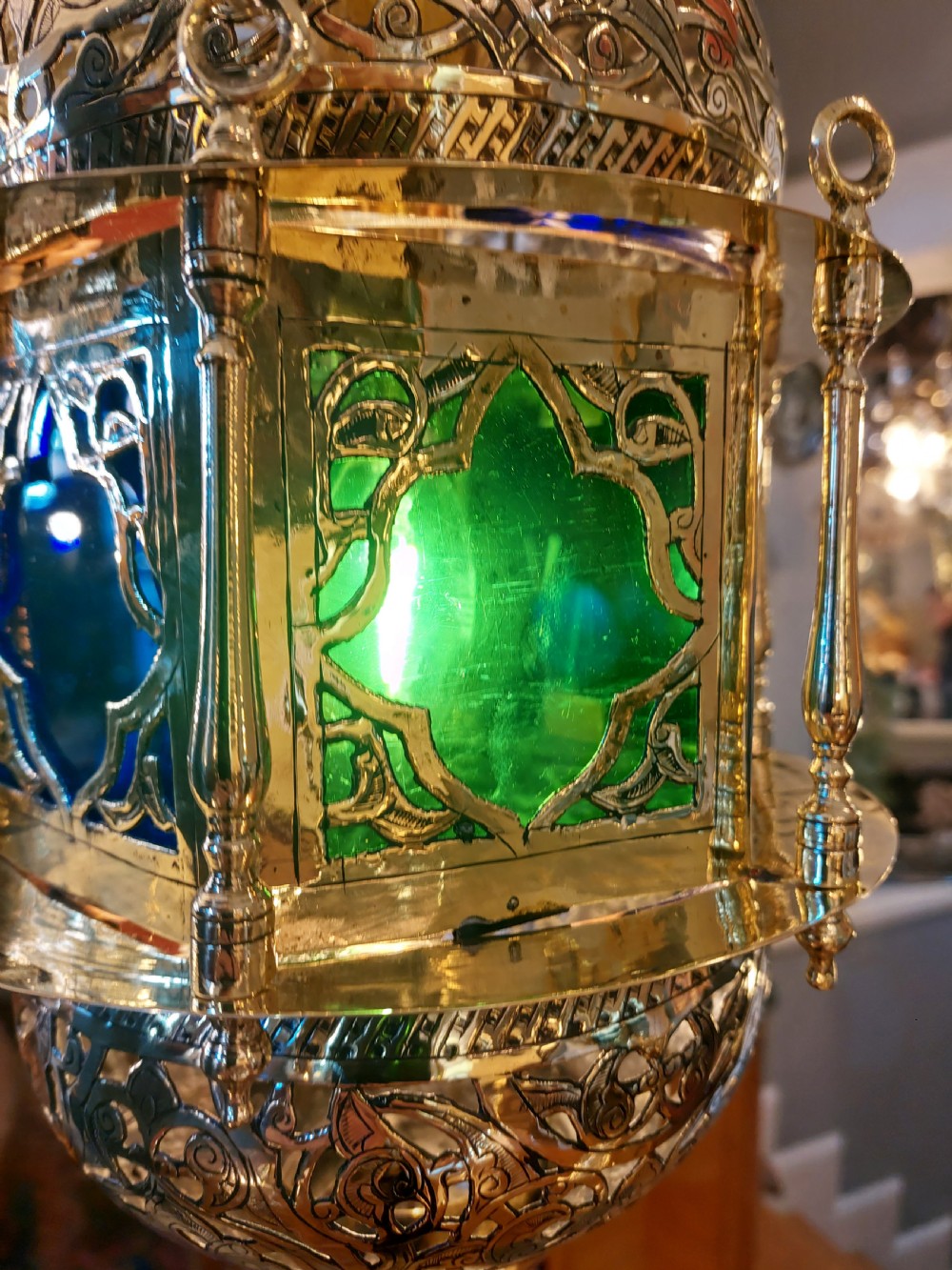 A hanging polished brass lantern featuring intricate pierced fretwork, dark glass insert panels, and three suspension chains topped with a crescent moon motif. View XII