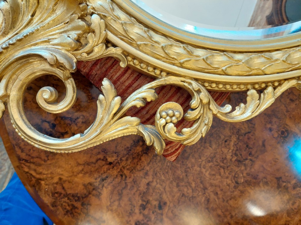 An oval giltwood wall mirror with carved cresting featuring a torch, quiver of arrows, and leaf garlands above an acanthus scroll base. View VIII