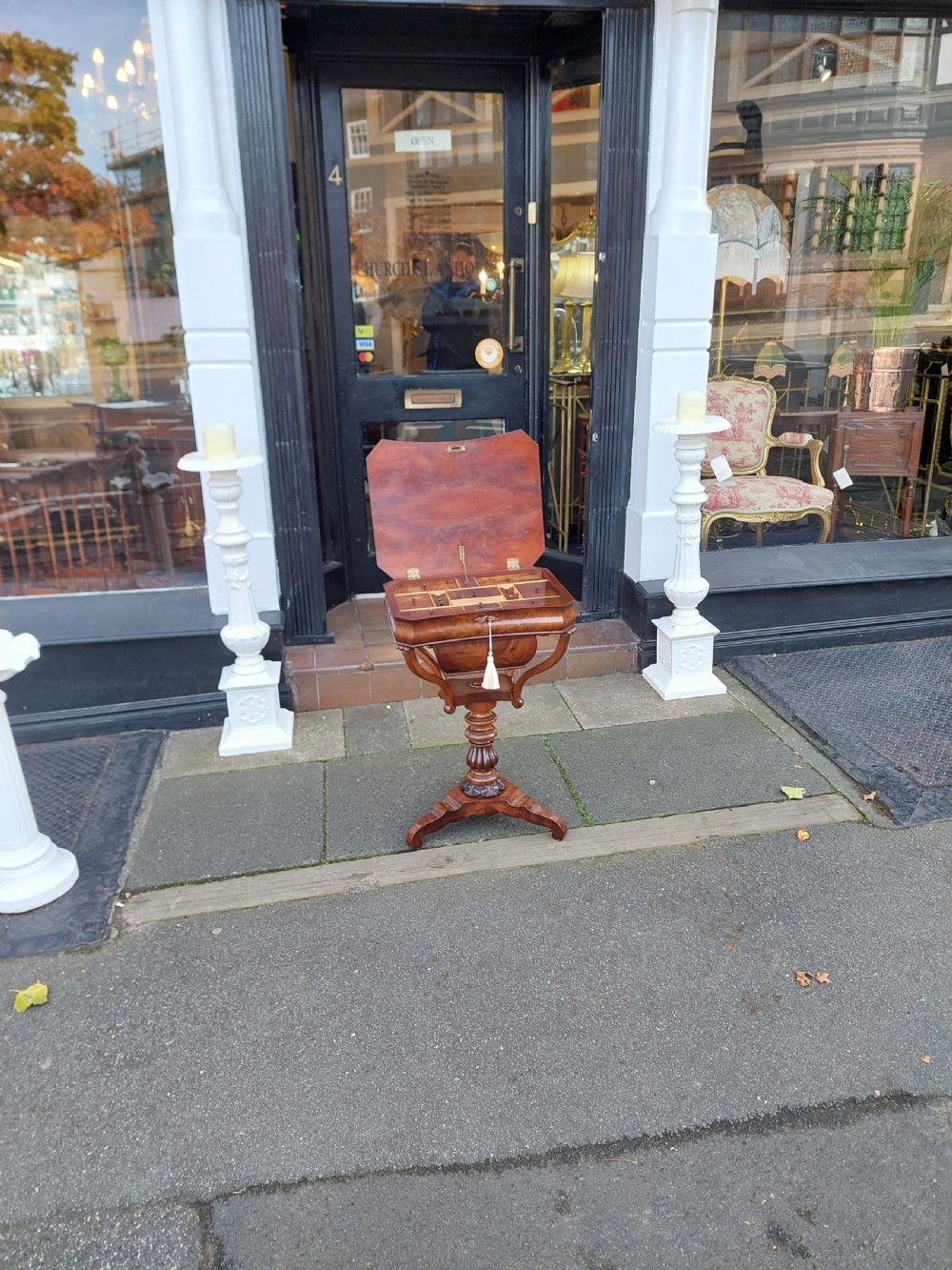 A flame mahogany Victorian sewing table featuring a canted corner top, a faceted turned pedestal column, and a scroll-cut tripod base. View II