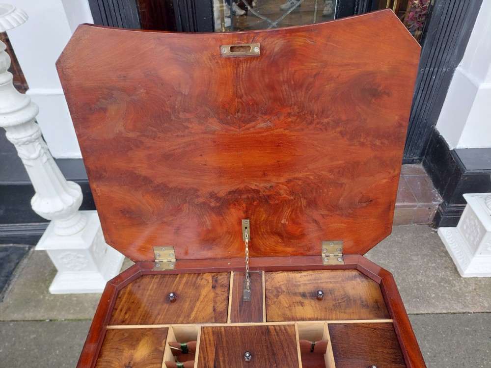 A flame mahogany Victorian sewing table featuring a canted corner top, a faceted turned pedestal column, and a scroll-cut tripod base. View IV