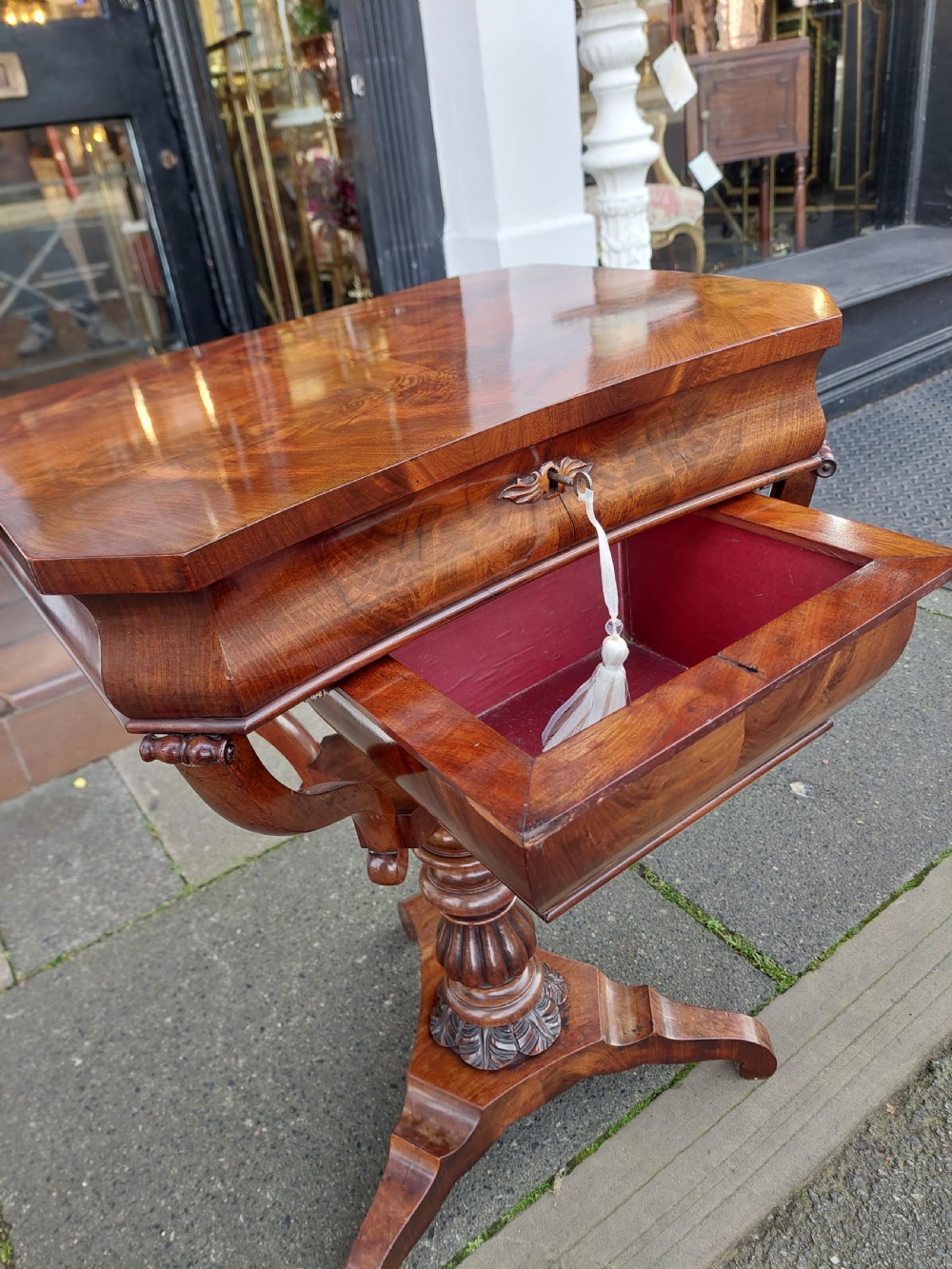 A flame mahogany Victorian sewing table featuring a canted corner top, a faceted turned pedestal column, and a scroll-cut tripod base. View IX